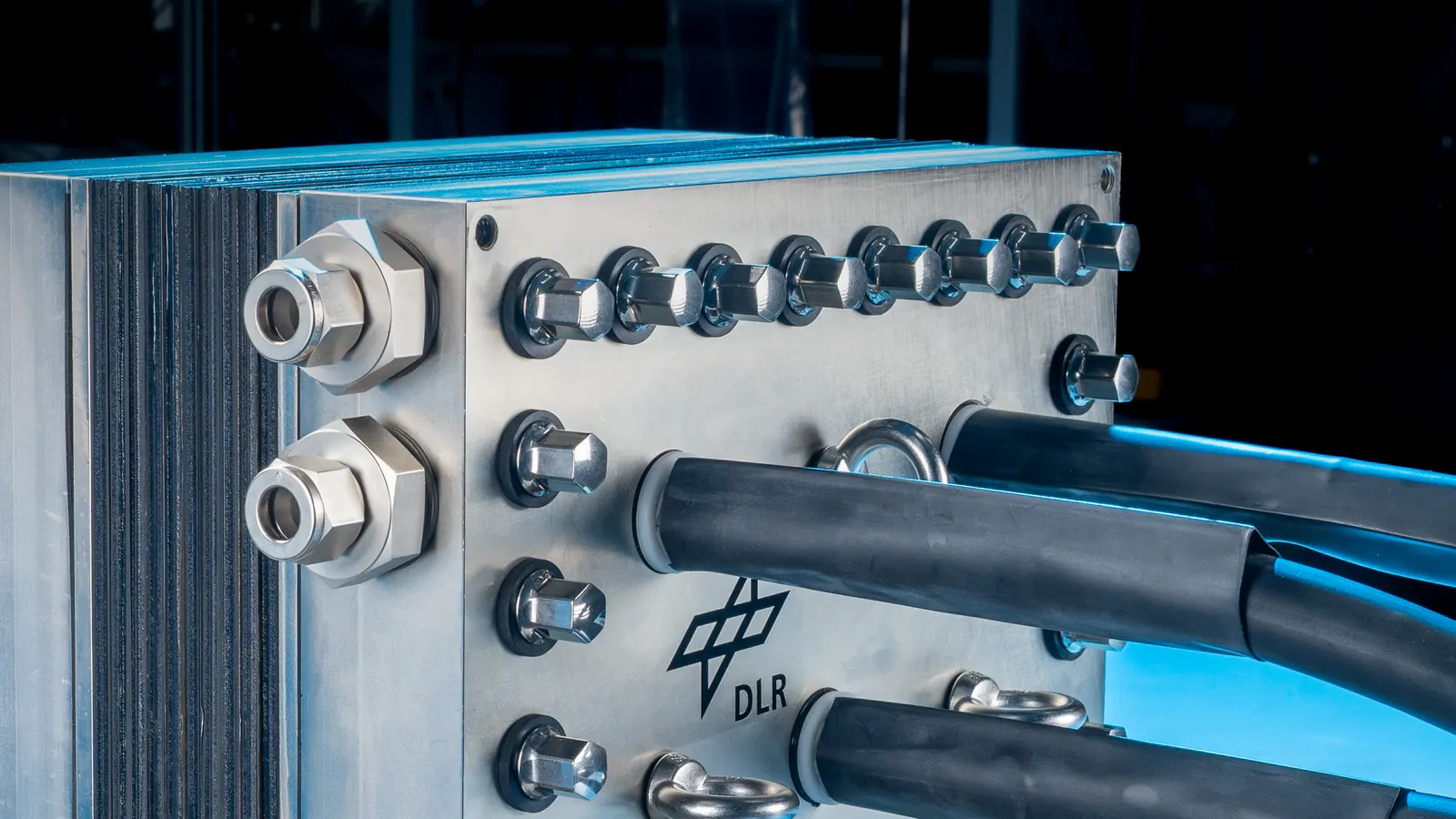 Detail of an electrolyser stack end plate with compression fittings, bolts and insulated hoses.