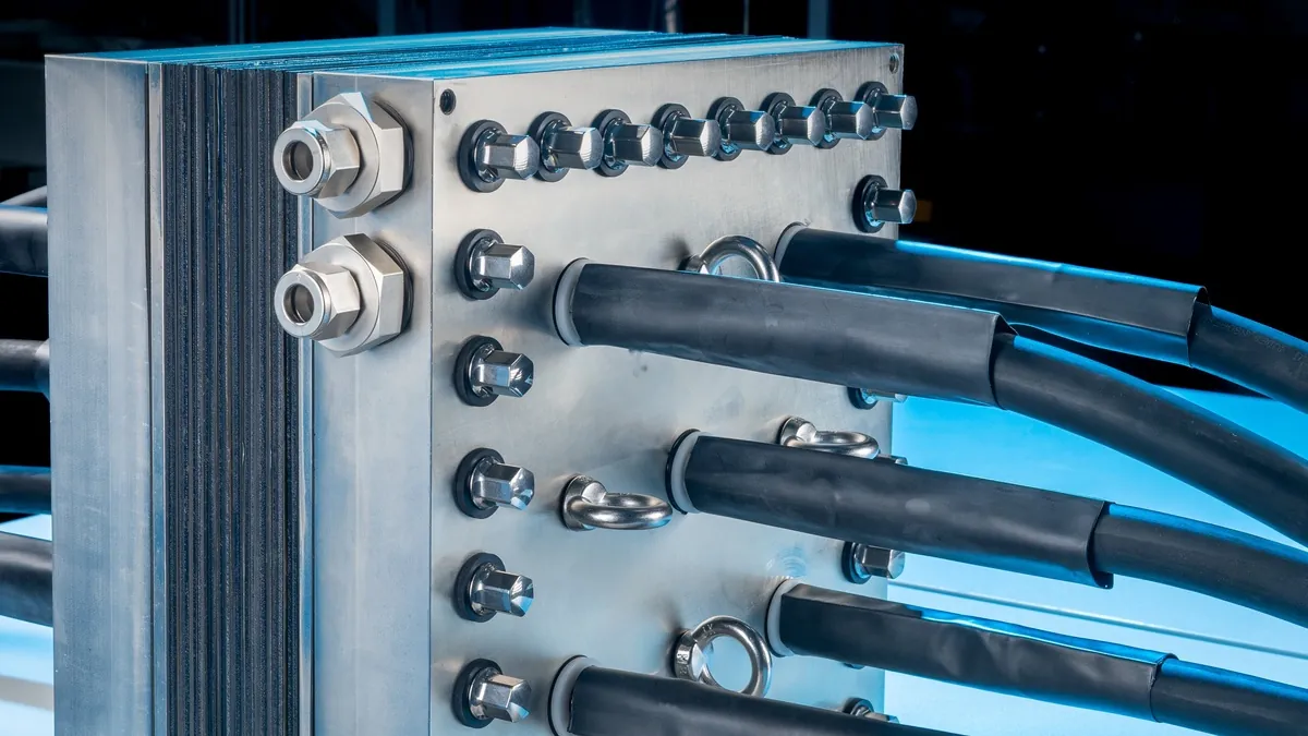 Close-up of an electrolyser stack end plate with fluid ports, bolts and power cable connections