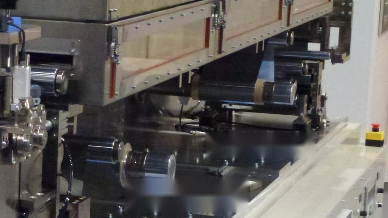 Detail of a roll-to-roll coating line with web-guiding rollers and dryer housing.