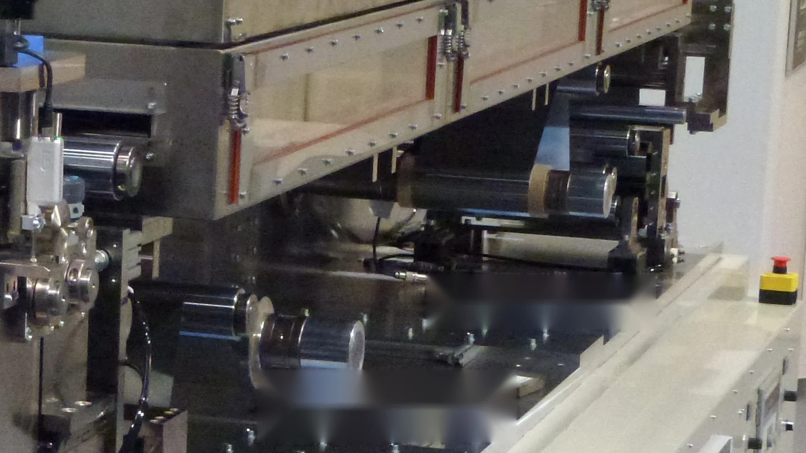 Detail of a roll-to-roll coating line with web-guiding rollers and dryer housing.