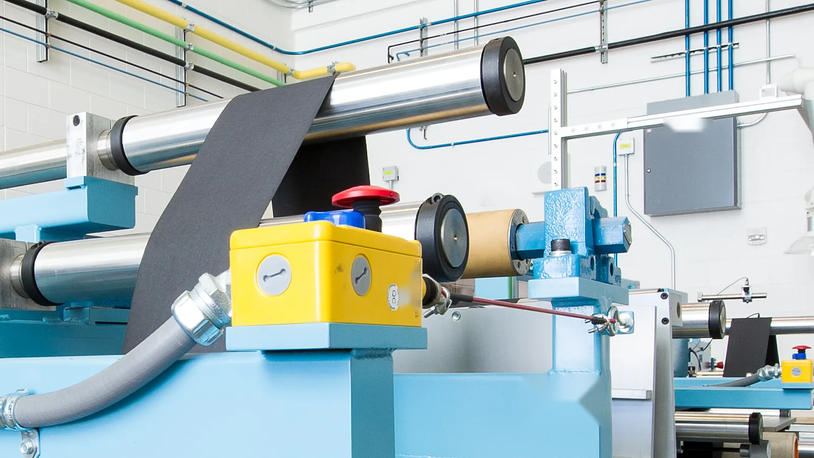 Roll-to-roll web line: precision rollers guide a dark film web between unwind and rewind stations.